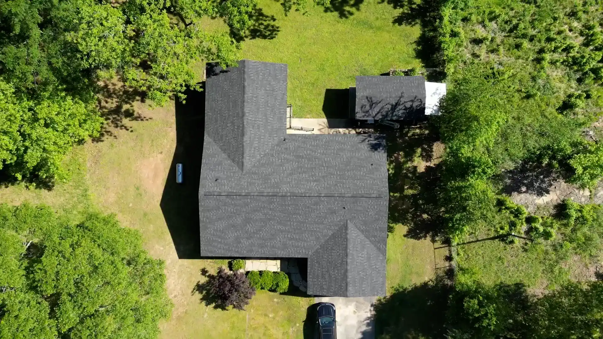 Aerial view of a dark shingle roof ringed by heavy tree canopy
